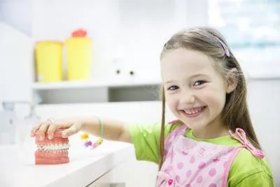 little girl smiling while playing with a model of teeth